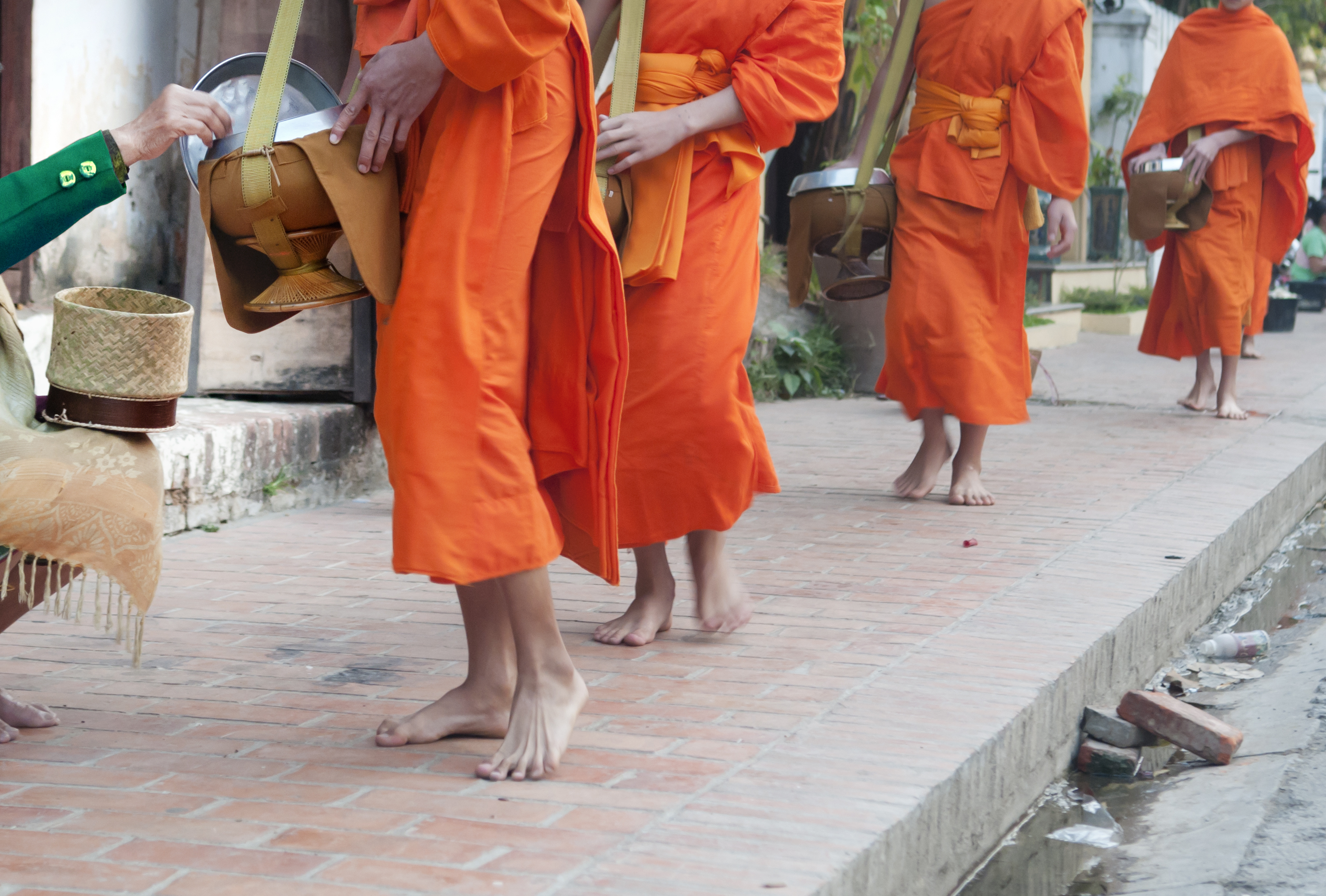 Monks wearing their traditional outfits, walking down the street collecting offerings from villagers